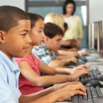 Elementary Students Working At Computers In Classroom Using Keyboard Concentrating