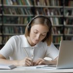 Serious student girl listening to audio tutorials from wireless headphones,