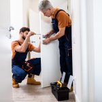 Best men at work. Full length shot of two locksmith, repairmen, workers in uniform installing, working with house door lock using screwdriver.