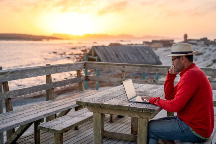 A man working on a laptop outdoors at the beach. A man working on a laptop outdoors at the beach.