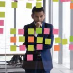 Young pensive Indian businessman in suit stand near glass wal