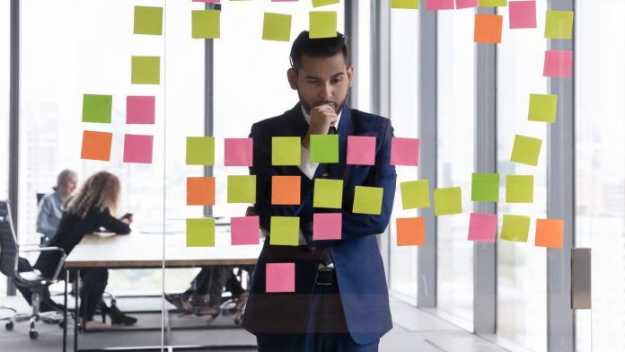 Young pensive Indian businessman in suit stand near glass wal