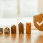 Wooden house model and real estate insurance ideas, and small shield icon.