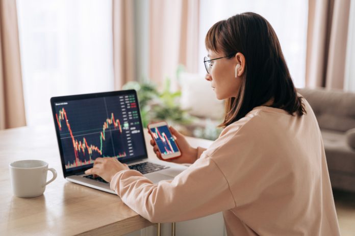 Female trader looking at laptop while holding smartphone