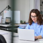 Woman employee sitting at desk working online on laptop