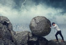 Business man pushing large stone up to hill