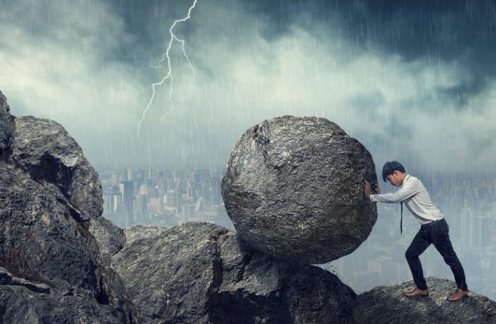 Business man pushing large stone up to hill