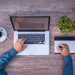 Top view of a man working on a laptop while drinking coffee