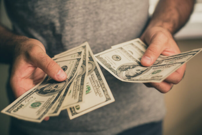 A man in a gray T-shirt holds dollars in his hands. Bank. Casino. Salary. Rates