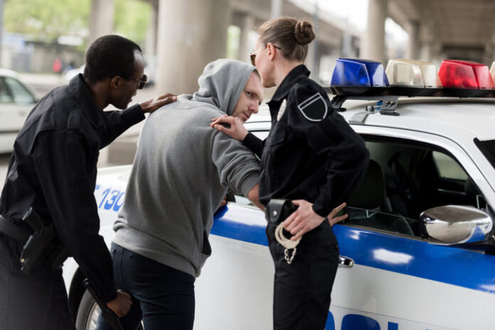 Policeman and policewoman arresting young man in hoodie