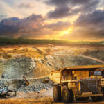 Yellow dump truck loading minerals copper, silver, gold, and other at mining quarry.