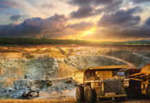 Yellow dump truck loading minerals copper, silver, gold, and other at mining quarry.