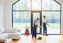 Young cleaners in blue uniform mopping wooden floor and cleaning big panoramic window