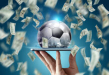 Dollars are falling on the background of a hand with a smartphone and a soccer ball