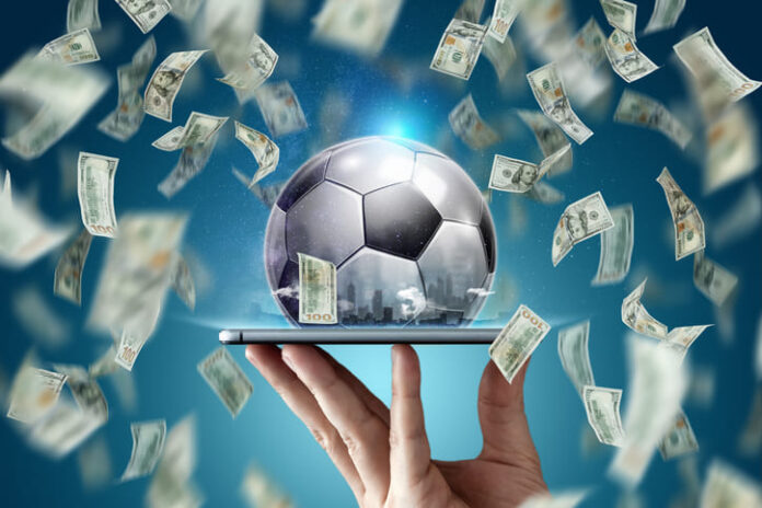 Dollars are falling on the background of a hand with a smartphone and a soccer ball