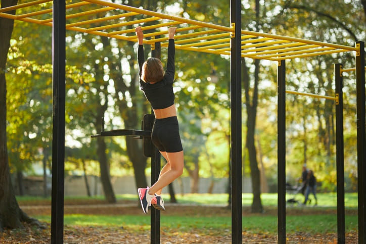 Woman crossing on horizontal bar during outdoors activity 