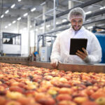 Technologist standing in food processing factory and checking quality of apple fruit.