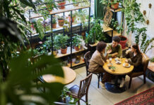 Two intercultural friends or dates having chat in cafe while sitting by table next to young woman drinking latte and listening to their discussion