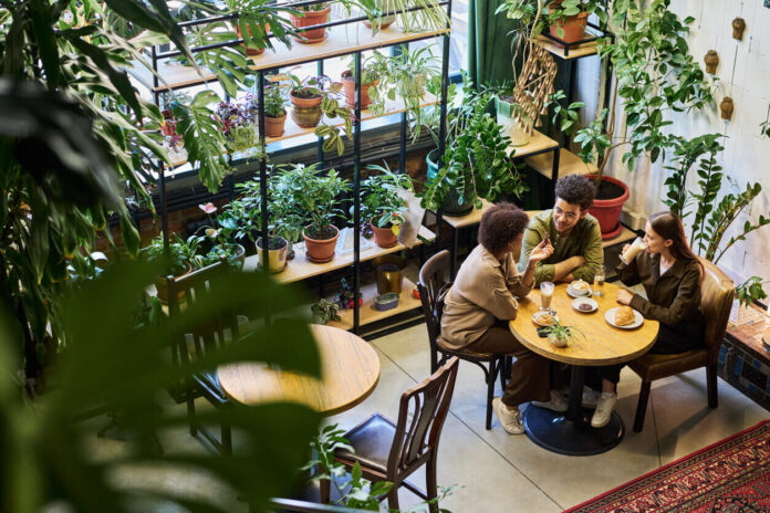 Two intercultural friends or dates having chat in cafe while sitting by table next to young woman drinking latte and listening to their discussion