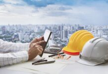 Hand of business man touching on computer tablet screen and safety helmet on working table against cities of high building