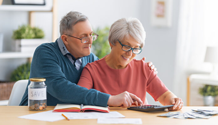 Elderly married couple sitting at the desk with a paper receipt in hands are calculating expenses, managing the budget.