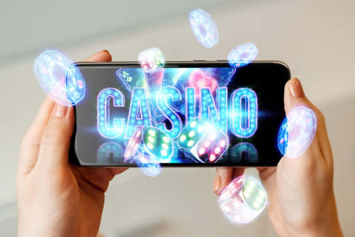 In a man's hand a smartphone with playing neon cards, chips, dice