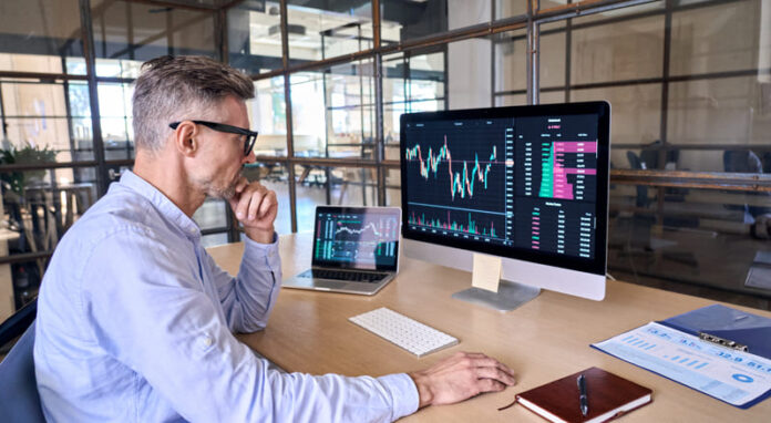 Trader using computer analyzing digital stock market trading graph.