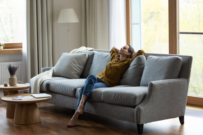 Happy carefree young female homeowner resting on comfortable couch.