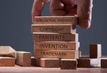 Man adding a block showing the words Intellectual property on top of other wooden block