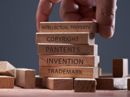 Man adding a block showing the words Intellectual property on top of other wooden block