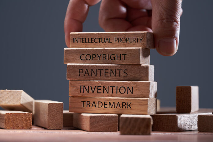 Man adding a block showing the words Intellectual property on top of other wooden block