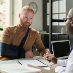 Portrait of man with hand in sling talking to insurance broker after workplace injury or accident