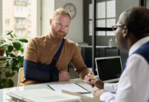 Portrait of man with hand in sling talking to insurance broker after workplace injury or accident