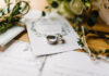 Stylish rings, flowers on wooden table background.