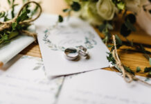 Stylish rings, flowers on wooden table background.