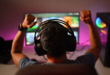 Back view of professional gamer wearing headphones celebrating victory while playing online video game at home