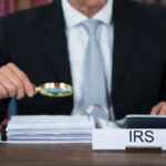 Midsection of tax auditor examining documents with magnifying glass at table in office