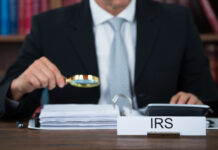 Midsection of tax auditor examining documents with magnifying glass at table in office