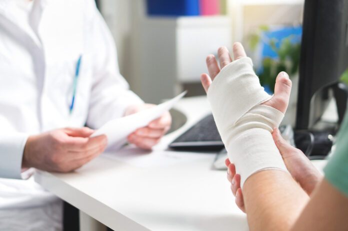 Injured patient showing doctor broken wrist and arm with bandage in hospital office or emergency room