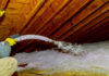 Technician spraying blown Fiberglass Insulation between Attic Trusses foam insulation construction foam from the gun to the roof