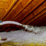 Technician spraying blown Fiberglass Insulation between Attic Trusses foam insulation construction foam from the gun to the roof