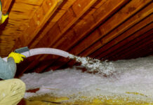 Technician spraying blown Fiberglass Insulation between Attic Trusses foam insulation construction foam from the gun to the roof