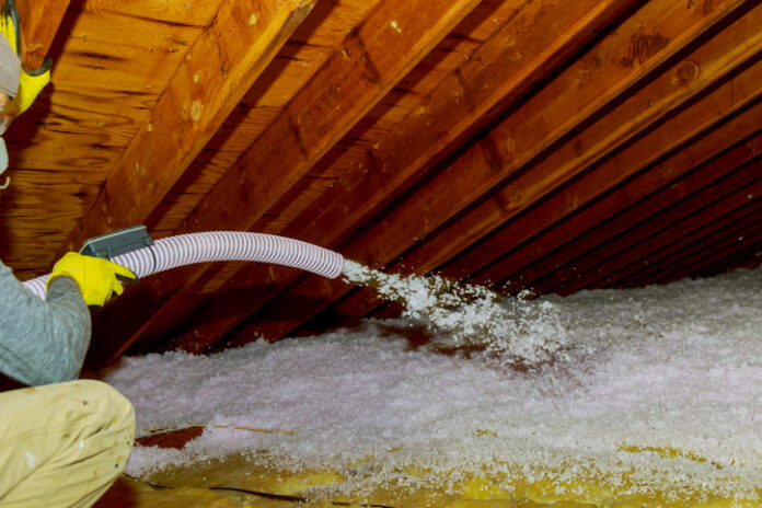 Technician spraying blown Fiberglass Insulation between Attic Trusses foam insulation construction foam from the gun to the roof