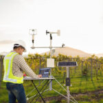 Agronomist using tablet computer collect data with meteorological instrument to measure the wind speed, temperature and humidity and solar cell system in grape agricultural field