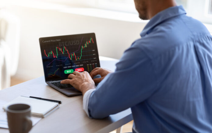 businessman working on laptop, sitting at desk in office, typing on keyboard, trading online, buying or selling bitcoins, cryptocurrency,