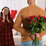 Man hiding bouquet of red roses for his beloved woman at home on Valentine's day celebration