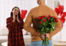 Man hiding bouquet of red roses for his beloved woman at home on Valentine's day celebration