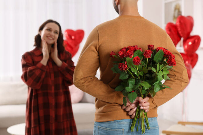 Man hiding bouquet of red roses for his beloved woman at home on Valentine's day celebration