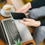 Person Using Smartphone and Laptop in Office Setting