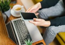 Person Using Smartphone and Laptop in Office Setting